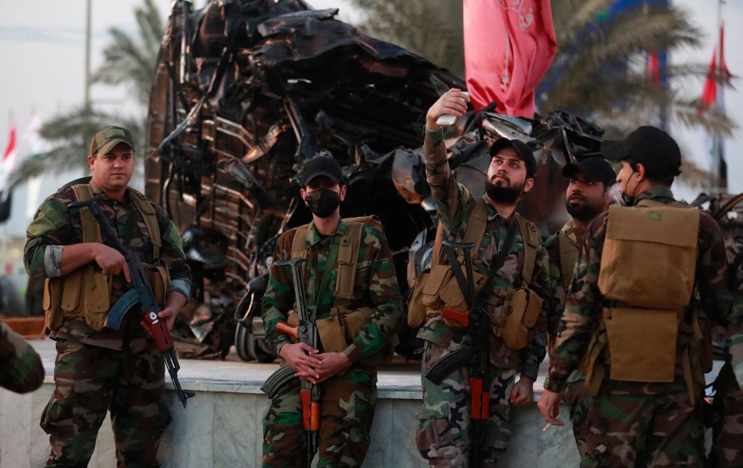 Members of the Popular Mobilization Forces (PMF or Hashd al-Shaabi) take photos in front of the wreckage of the car in which Iranian general Qasem Soleimani and Iraqi militia commander Abu Mahdi al-Muhandis were killed, near Baghdad airport on January 2, 2021. Photo: AFP
