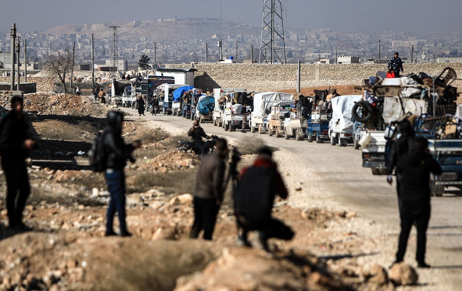 People watch as a convoy of trucks transports internally displaced Syrians east of the city of al-Bab in the northern Aleppo governorate on February 9, 2022. Photo: Bakr Alkasem/AFP
