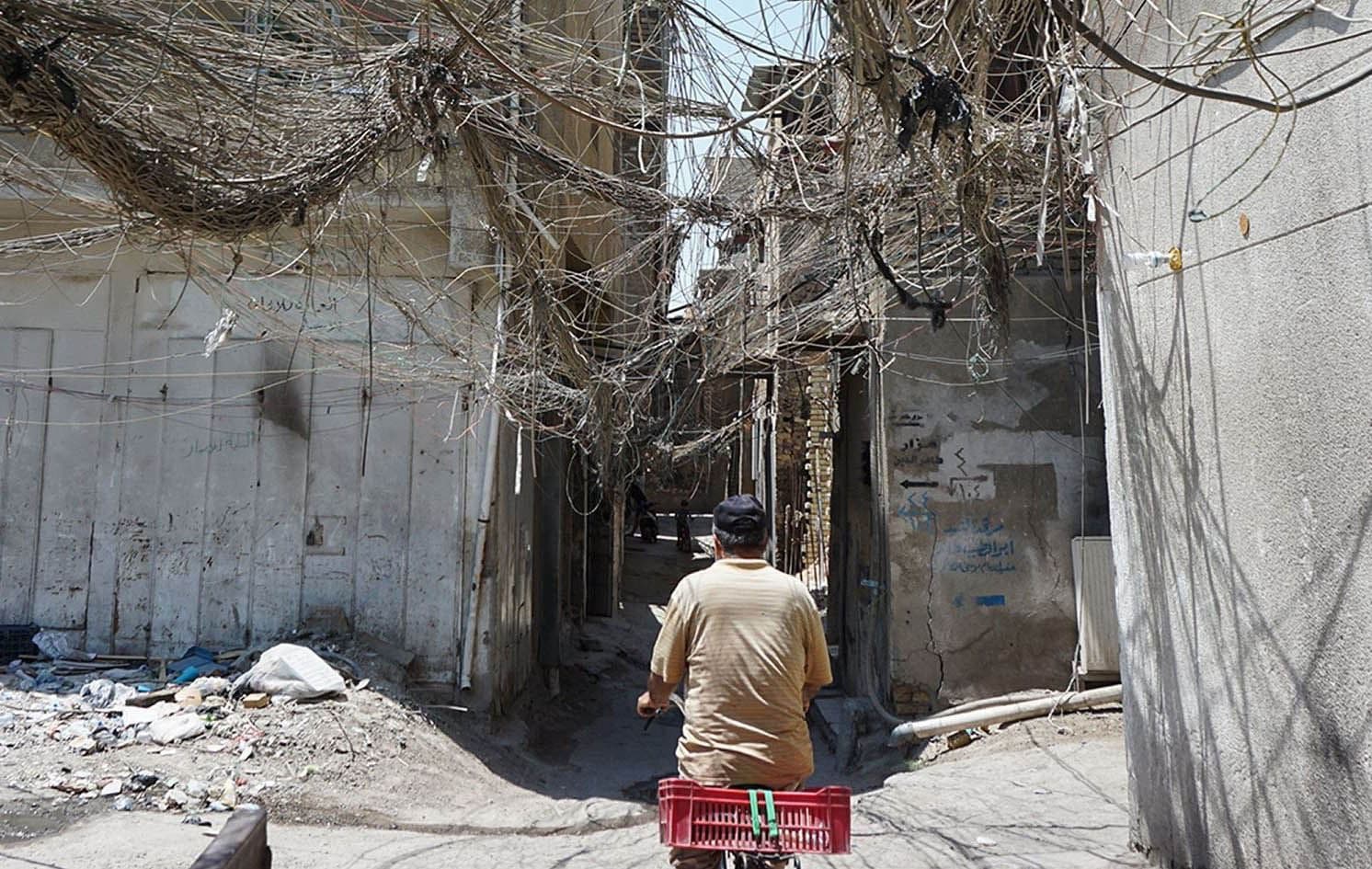 An Iraqi man rides a bicycle beneath a web of electricity wires in the Syed Sultan Ali area of Baghdad on July 13, 2020. File photo: Sabah Araf/AFP