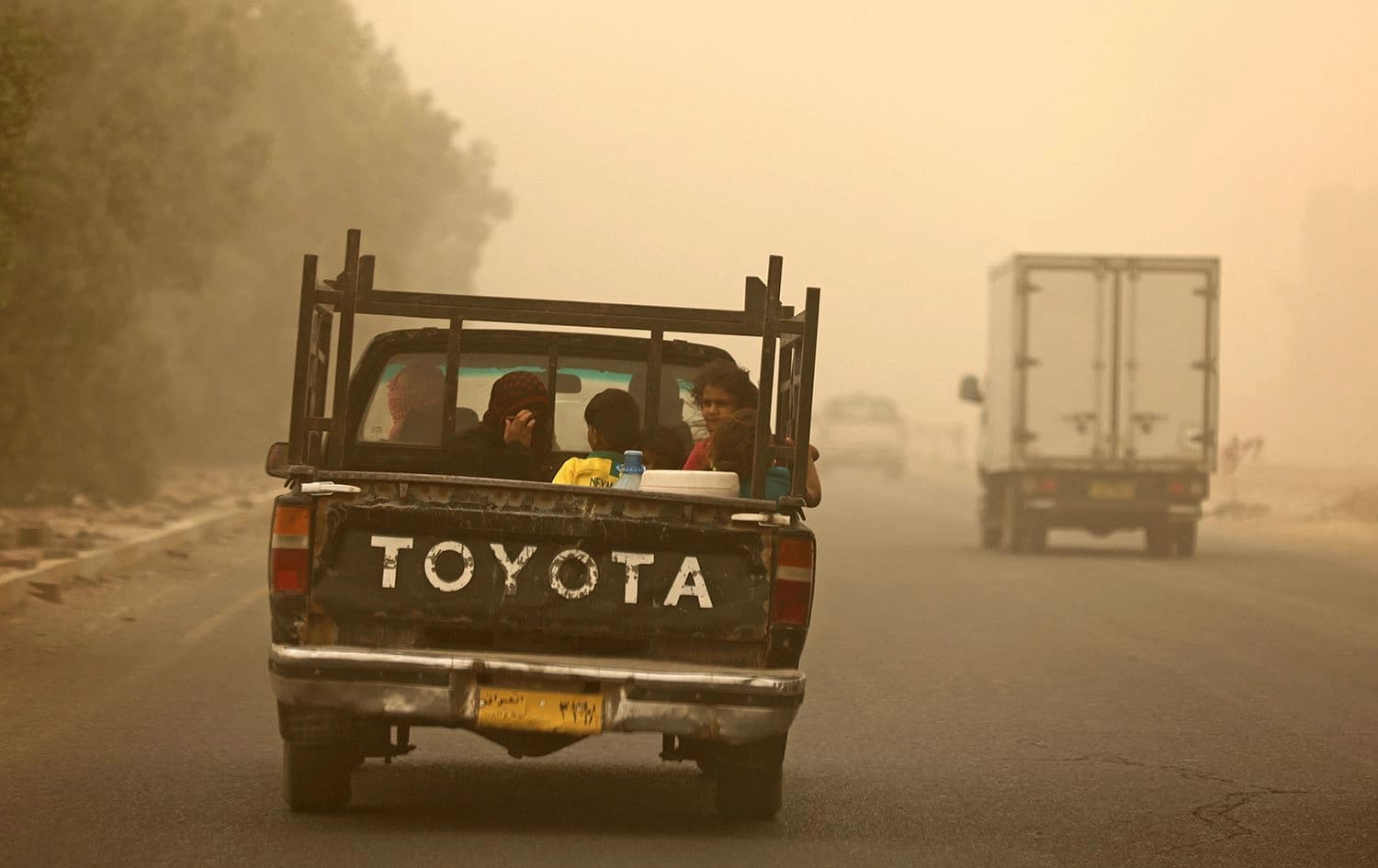 A family rides in the back of a pickup truck during a sandstorm in Diyala province on July 3, 2022. Photo: Ahmad al-Rubaye/AFP