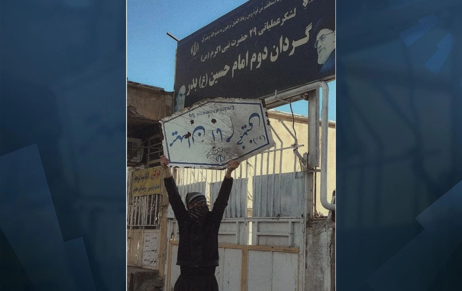 A defiant young man holds a street sign reading “Imam Khomeini”, the founder of the Islamic Republic, and stands outside the Islamic Revolutionary Guard Corps (IRGC) in the Kurdish town Javanrud, western Iran (Rojhelat) on December 31, 2022. Photo: Javanrud Telegram channels 