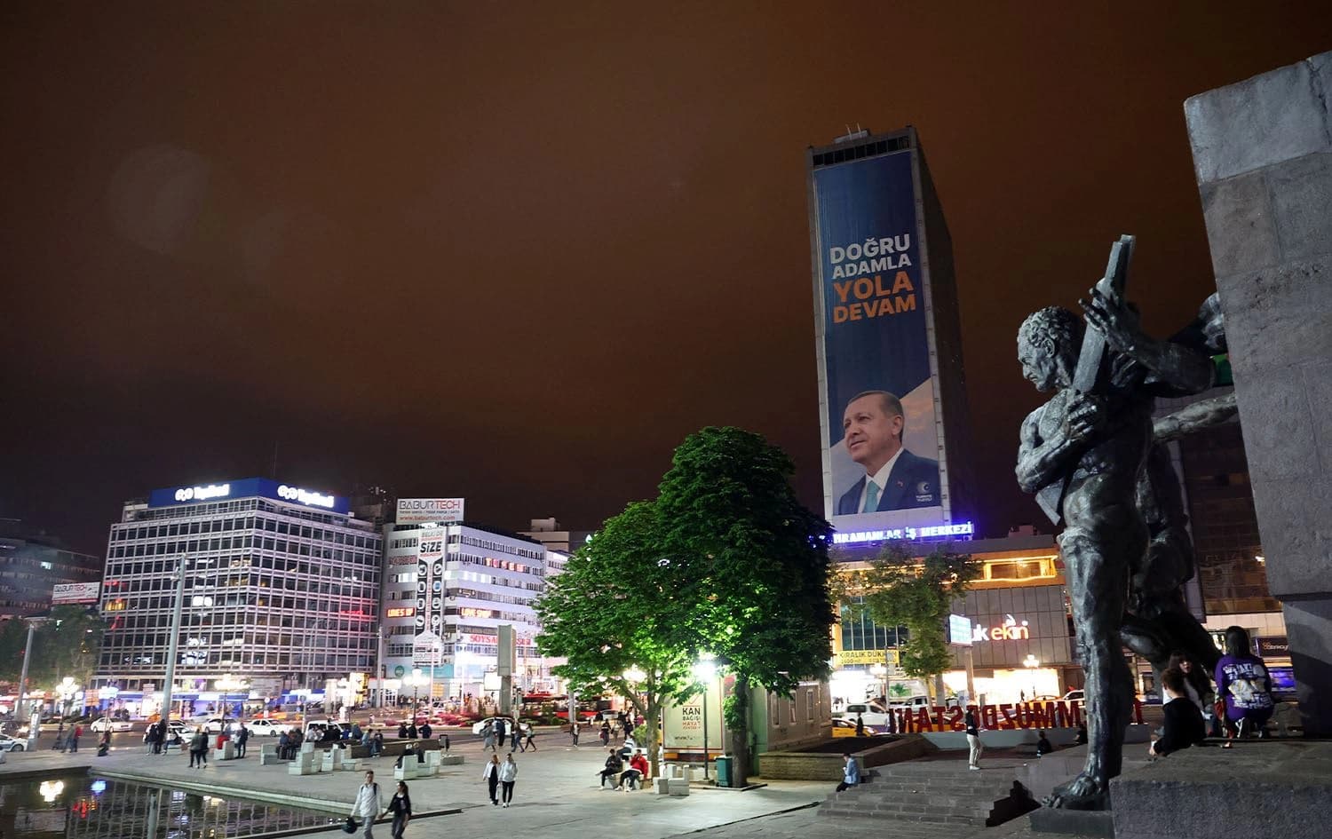 Pedestrians walk underneath a poster showing a portrait of Turkey's President Recep Tayyip Erdogan at Guven Park Monument in Kizilay Square, Ankara on May 27, 2023, on the eve of a runoff in Turkey's presidential election. Photo: Adem Altan/AFP