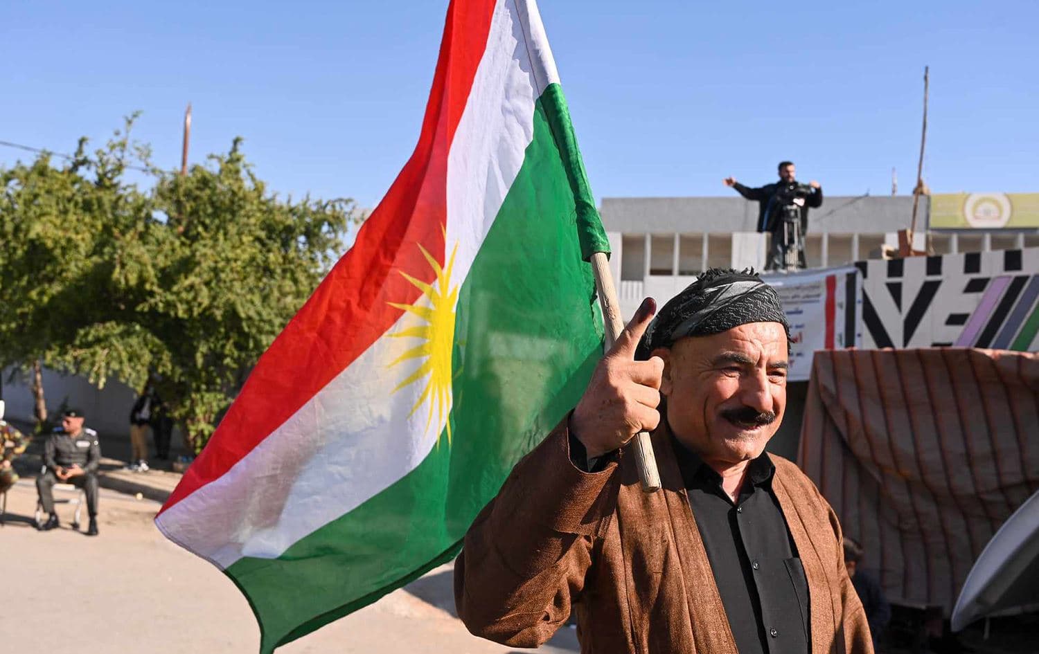 A man wearing traditional Kurdish clothing and carrying the Kurdistan Region flag shows his ink-stained finger after voting in Kirkuk's provincial council elections on December 18, 2023. Photo: Bilind T. Abdullah/Rudaw
