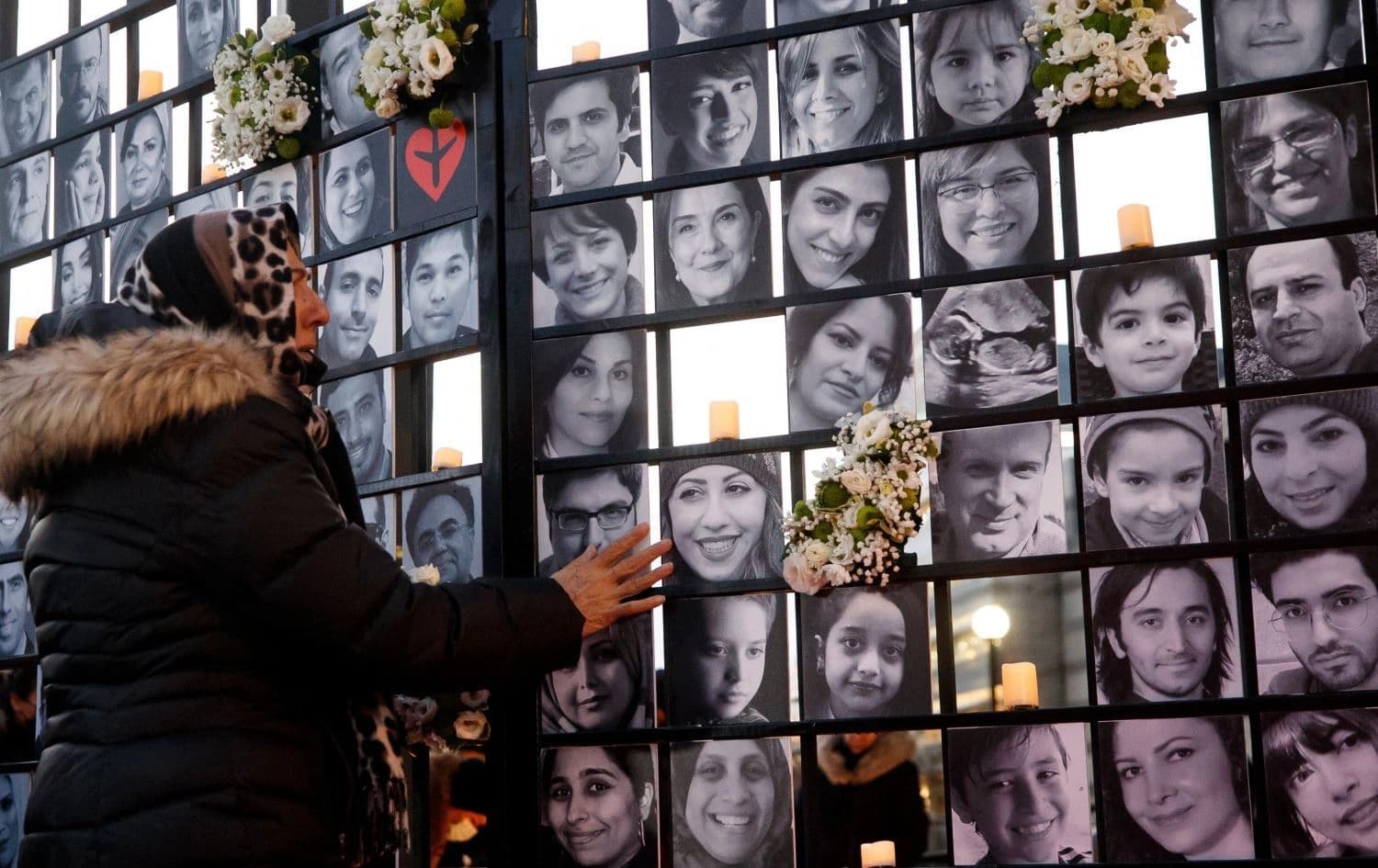 A woman touches victims' portraits as mourners attend an outdoor vigil for the victims of Ukrainian passenger jet PS752 on January 8, 2022. Photo: AFP