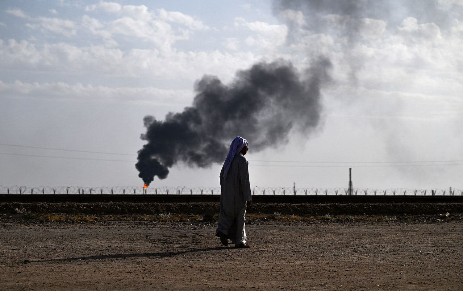 Local resident Hussein Julood walks in front of his house as smoke billows from gas flaring in the nearby Rumaila oil field in Iraq's southern province of Basra, on May 5, 2024. Photo: Hussein Faleh/AFP