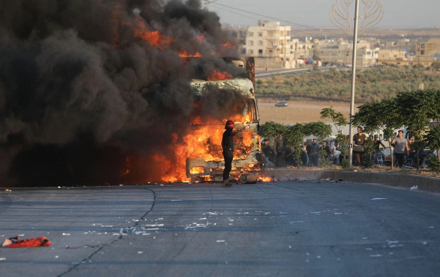 A protester stands in front a burning Turkish truck during protests against Turkey in al-Bab, in the northern Syrian opposition held region of Aleppo on July 1, 2024. Photo: Bakr ALKASEM / AFP