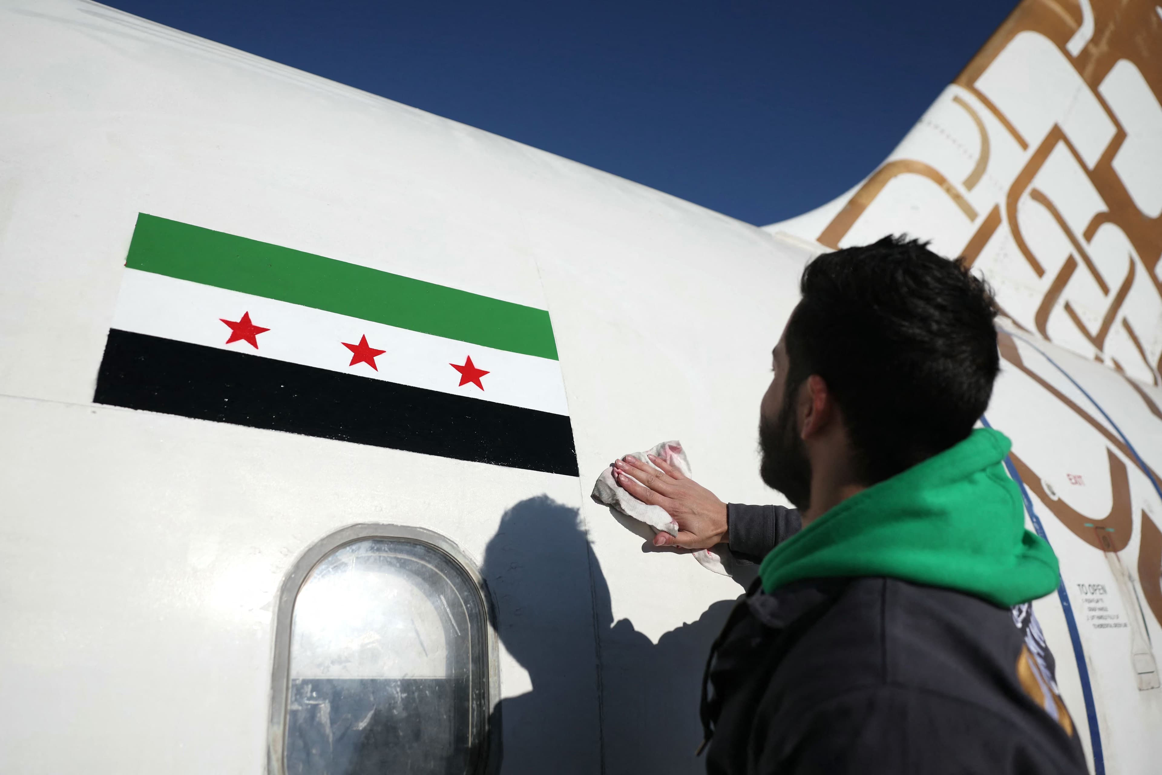 A man cleans after painting the flag of the Syrian revolution on a Cham Wings Airlines Airbus A320-231 aircraft at Damascus international airport as the new Syrian authorities prepare to reopen it, on December 16, 2024. Photo: AFP