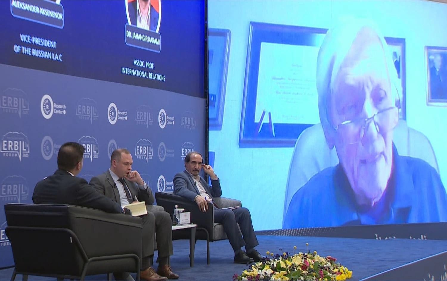 The senior research fellow at the Institute of World Economy and International Affairs Nikolay Surkov (center), an expert on Russia and a professor of international relations at the University of Tehran Jahangir Karami (right), and the vice president of the Russian International Affairs Council Ambassador Aleksander Aksenenok (on screen) attend the Erbil Forum 2025 on February 27, 2025. Photo:  screengrap/Rudaw