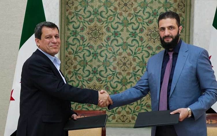 ئەحمەد شەرع و مەزڵووم عەبدی لەدوای واژۆکردنی رێککەوتنەکە تەوقە دەکەن. 
