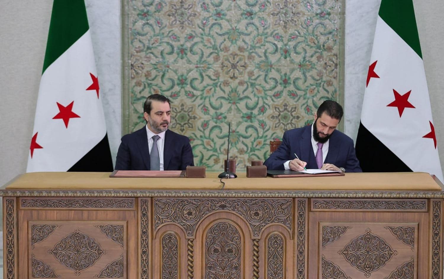 Syria's interim President Ahmed al-Sharaa (right) is accompanied by Foreign Minister Asaad al-Shaibani (left) as he signs Syria's constitutional declaration on March 13, 2025. Photo: SANA