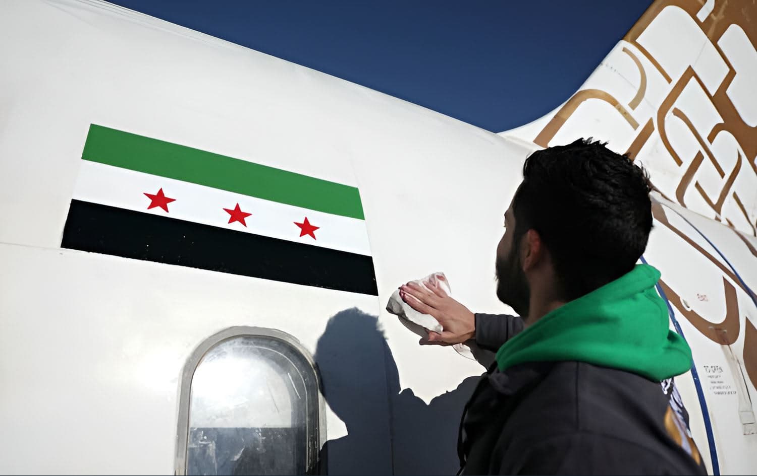 A man cleans after painting the flag of the Syrian revolution on a Cham Wings Airlines Airbus A320-231 aircraft at Damascus international airport as the new Syrian authorities prepare to reopen it, on December 16, 2024. Photo: AFP