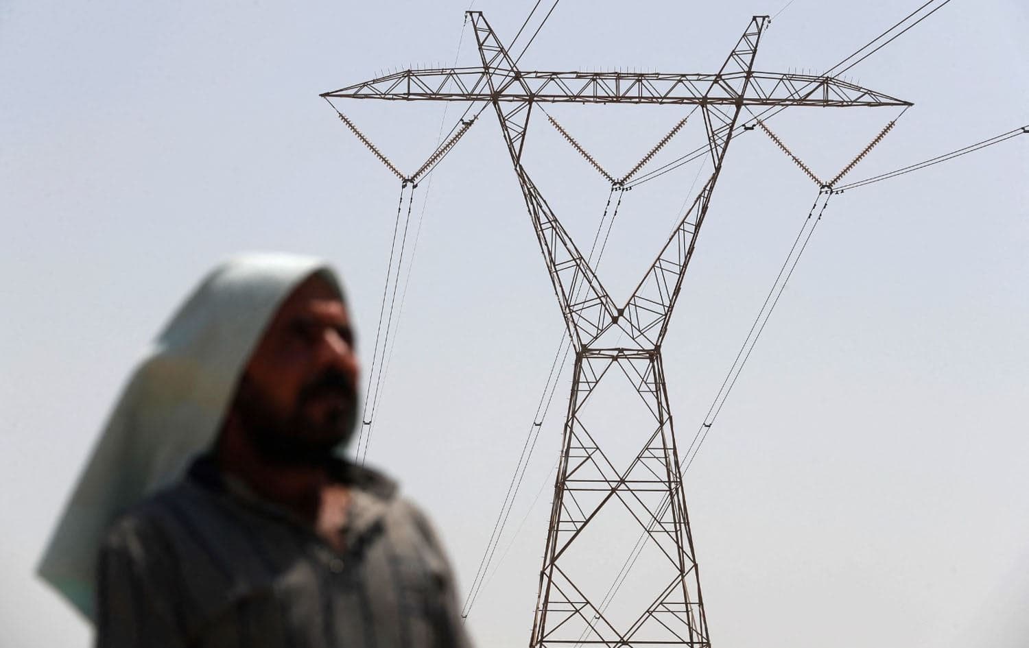 An Iraqi man stands under an electricity transmission tower south of Hilla city on August 10, 2025, amidst rising temperatures, chronic water shortages, and power cuts. Photo: Ahmad al-Rubaye/AFP