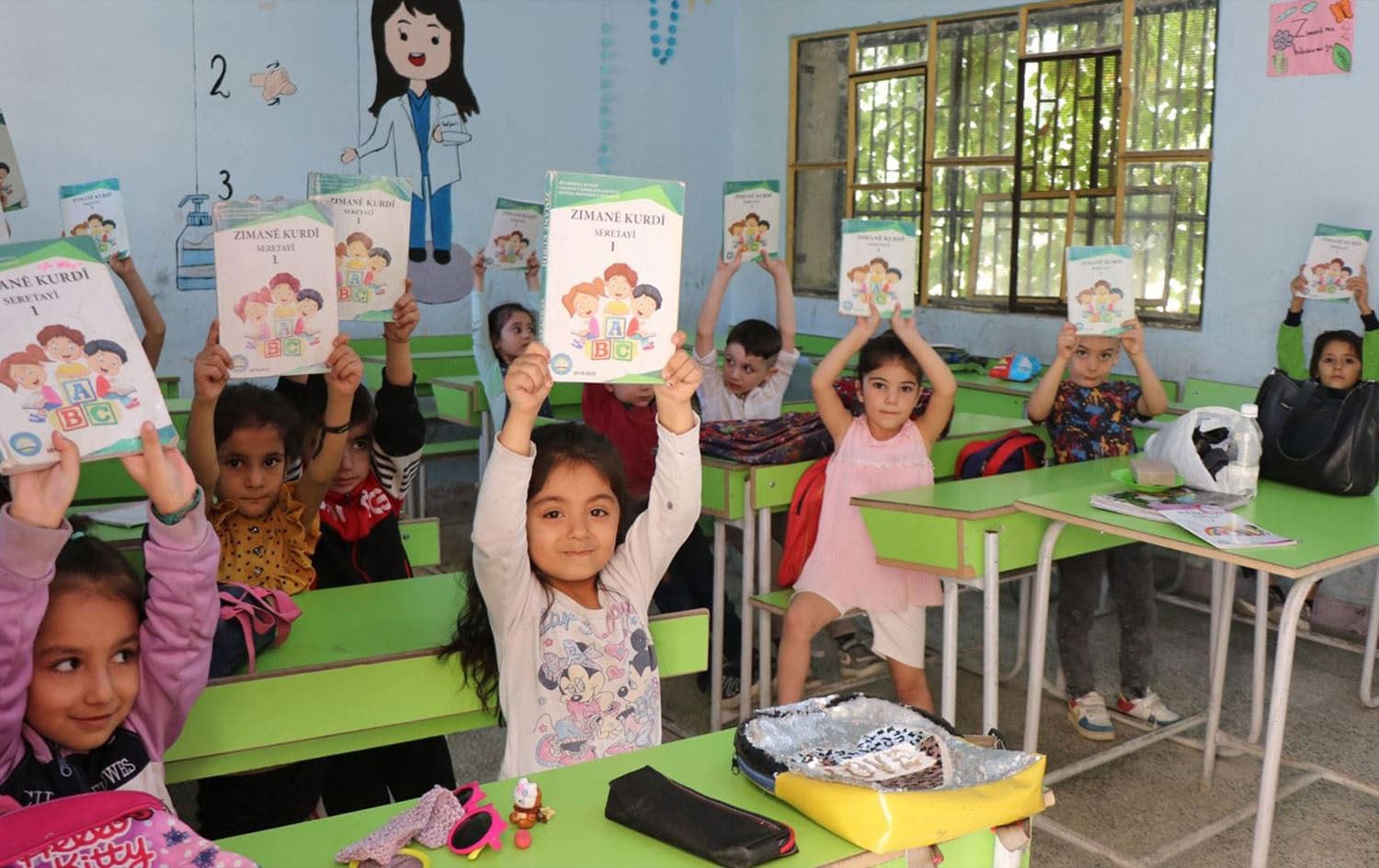 Students hold up Kurdish language books in a class in Rojava. Photo: ANHA/file