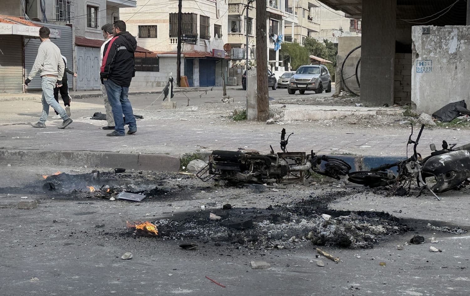 Residents standing close to a destroyed motorcycle on a street amid protests in Syria’s coastal areas: Photo: SANA