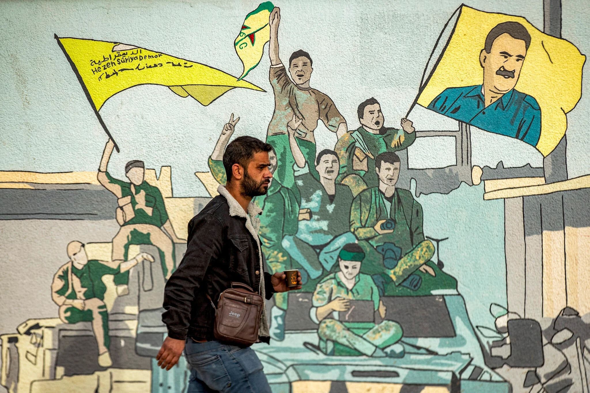 A man walks past a mural depicting supporters of the Syrian Democratic Forces (SDF), one of them raising a flag showing the face of Abdullah Ocalan, jaild leader of the Kurdistan Workers’ Party (PKK) in December 2014. Photo: AFP