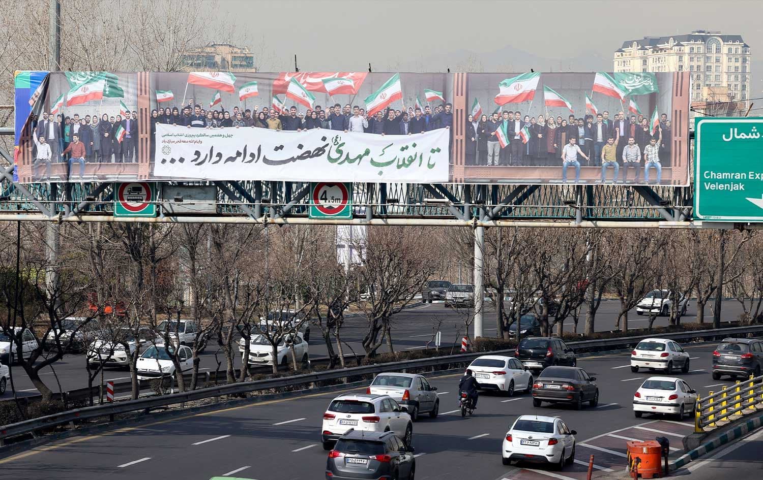 Vehicles drive along a highway under a pedestrian bridge with a huge banner showing people waving the Iranian flag, in Tehran on February 18, 2026. Photo: AFP