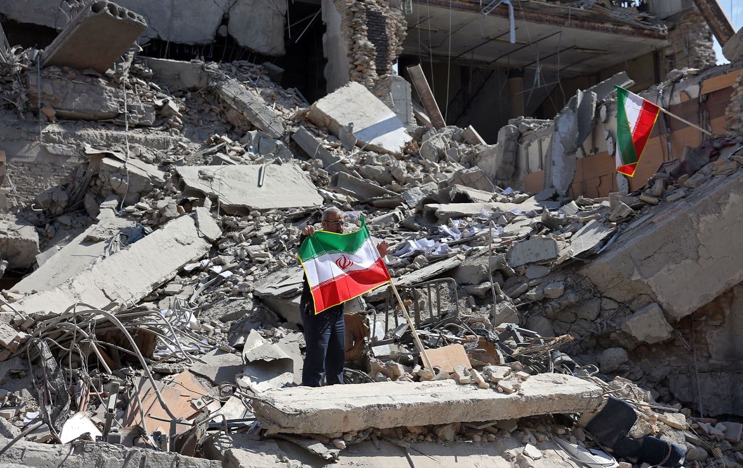 A man holds an Iranian flag amid the debris of a destroyed building following airstrikes in central Tehran on March 4, 2026. Photo: AFP