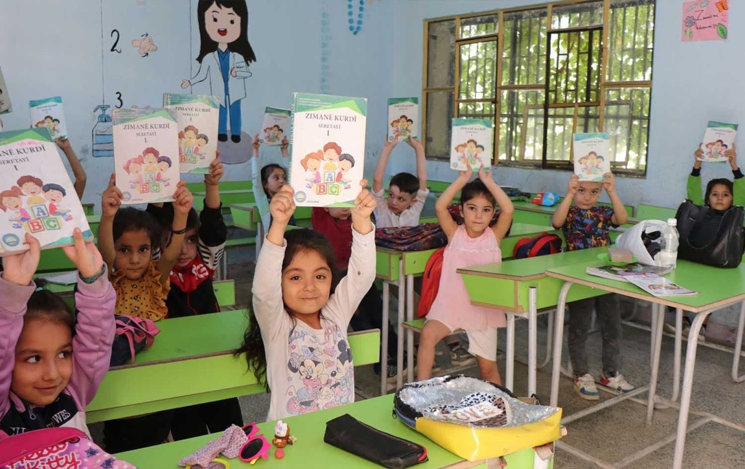Students hold up Kurdish language books in a class in Rojava. Photo: ANHA/file