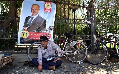 A man sits in front of an election campaign poster in Erbil the capital of the Kurdistan Region on April 24, 2018. Photo: Safin Hamed | AFP