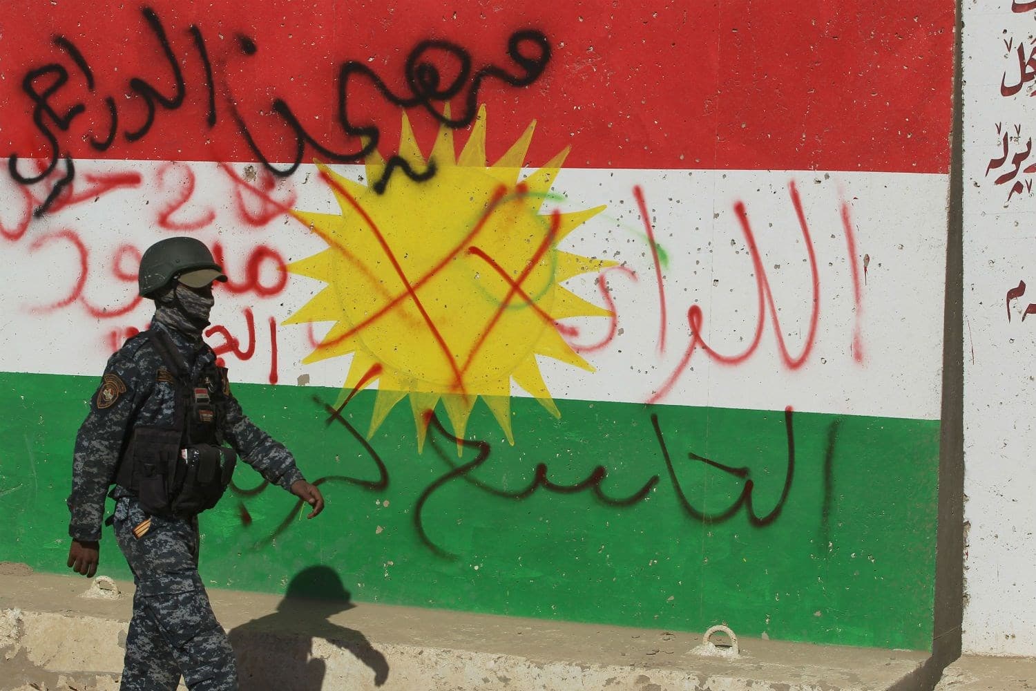 A member of the Iraqi Security Forces strolls by a defaced wall in Kirkuk displaying the Flag of Kurdistan on October 16, 2018. Photo: Ahmed al-Rubaye | AFP