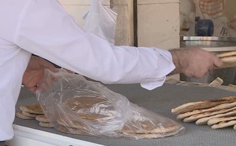 A baker in Sulaimani packs fresh bread into a plastic bag for a customer. Photo: Rudaw