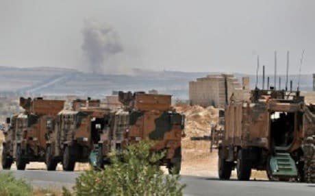 A Turkish military convoy advances through the Syrian province of Idlib on August 19, 2019. Smoke from reported Syrian and Russian airstrikes billows in the background. Photo: AFP/ Omar Haj Kadour