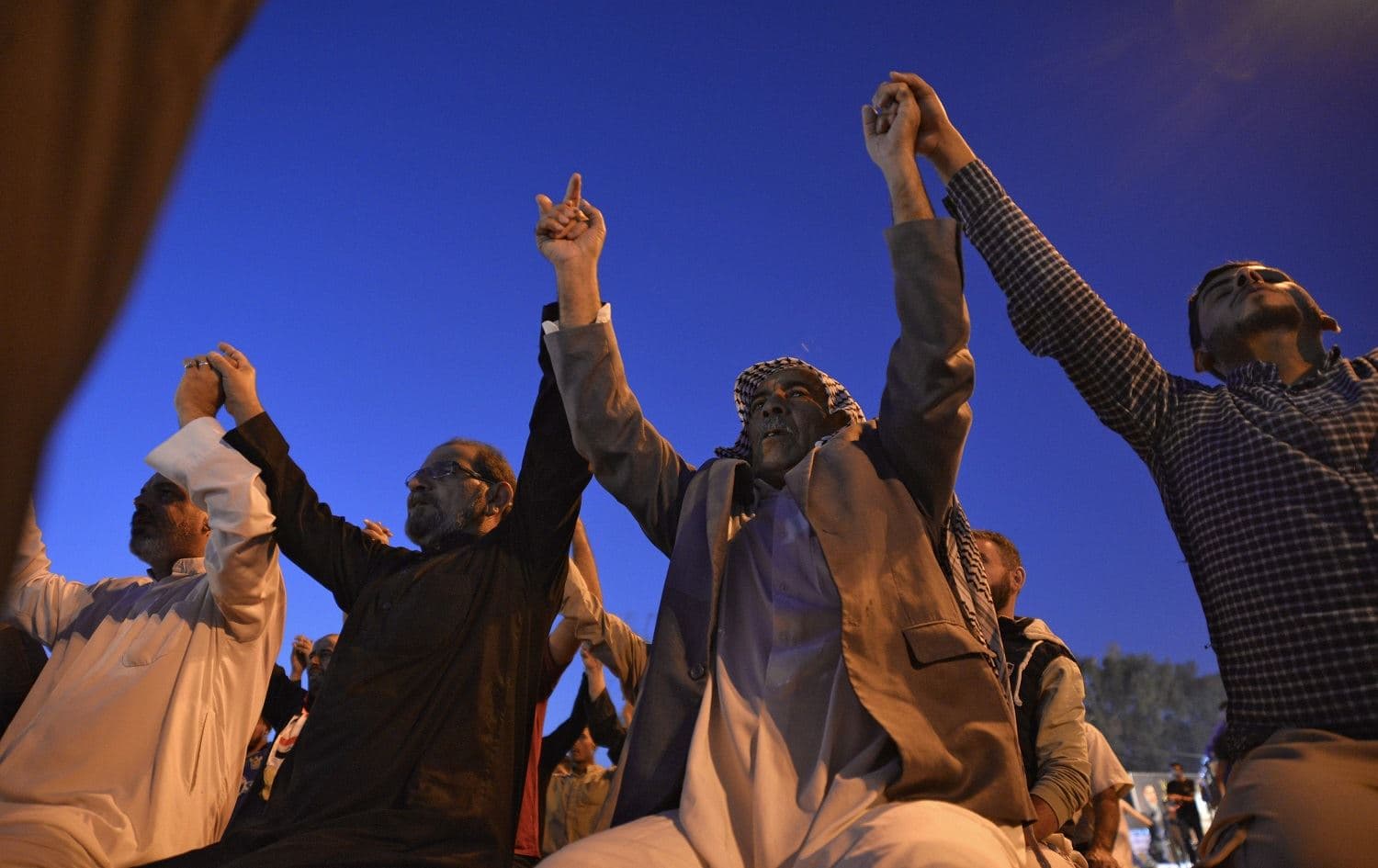 Iraqi protesters hold hands as a sign of unity after taking part in collective prayers during ongoing anti-government demonstrations in the central holy shrine city of Najaf on November 10, 2019. Photo: AFP / Haidar Hamdani