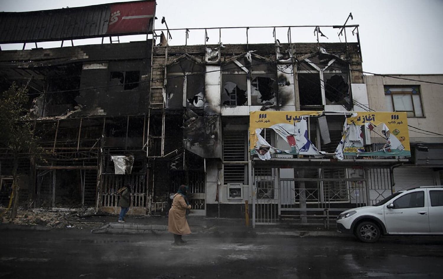 In this photo taken Monday, Nov. 18, 2019, people walk past buildings which burned during protests in the Iranian city of Karaj. Photo: Masoume Aliakbar/ISNA via AP