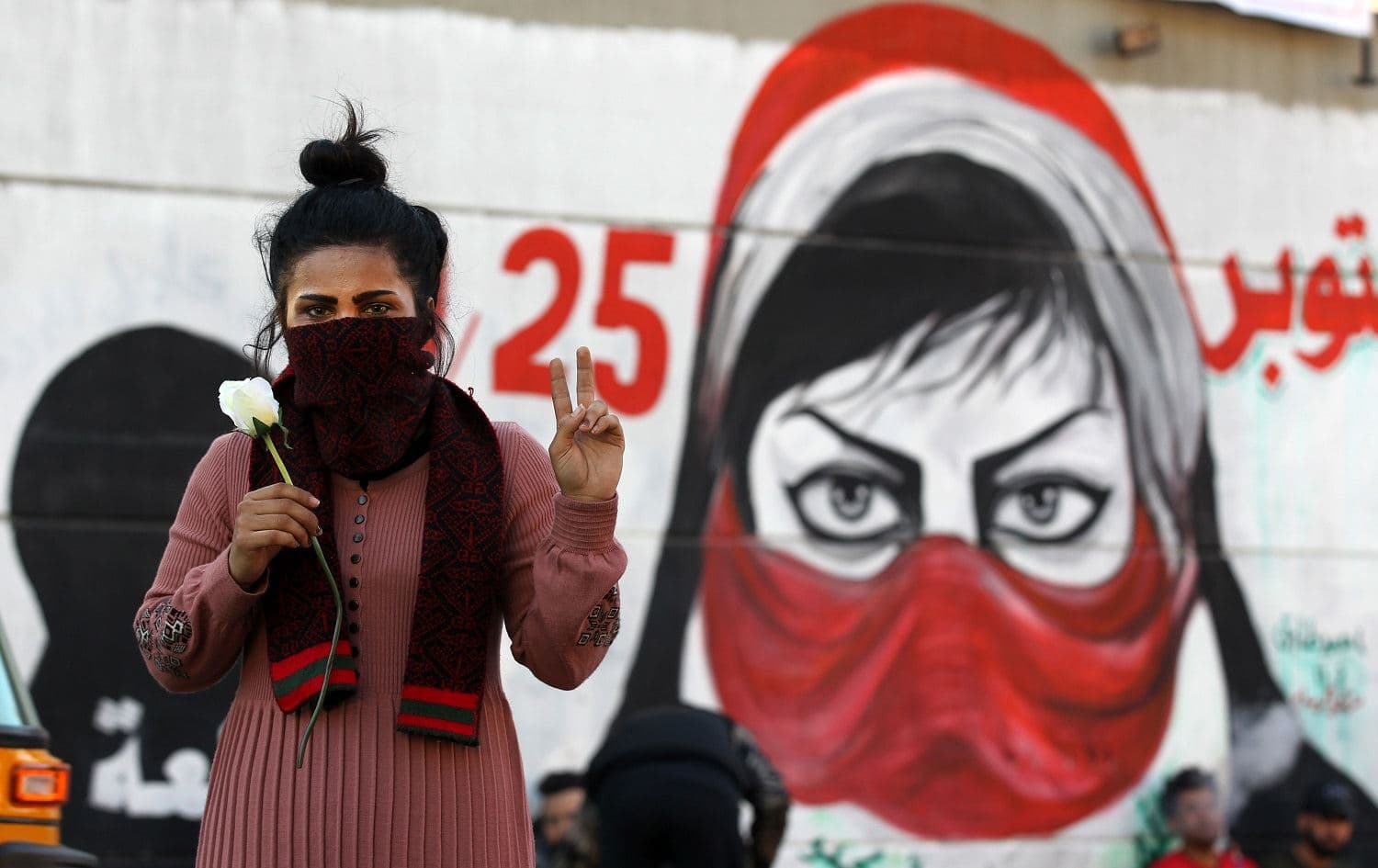 An Iraqi woman flashes the victory sign in front of a mural in Baghdad's Tahrir square amid ongoing anti-government demonstrations on December 19, 2019. Photo: Ahmad Al-Rubaye/AFP