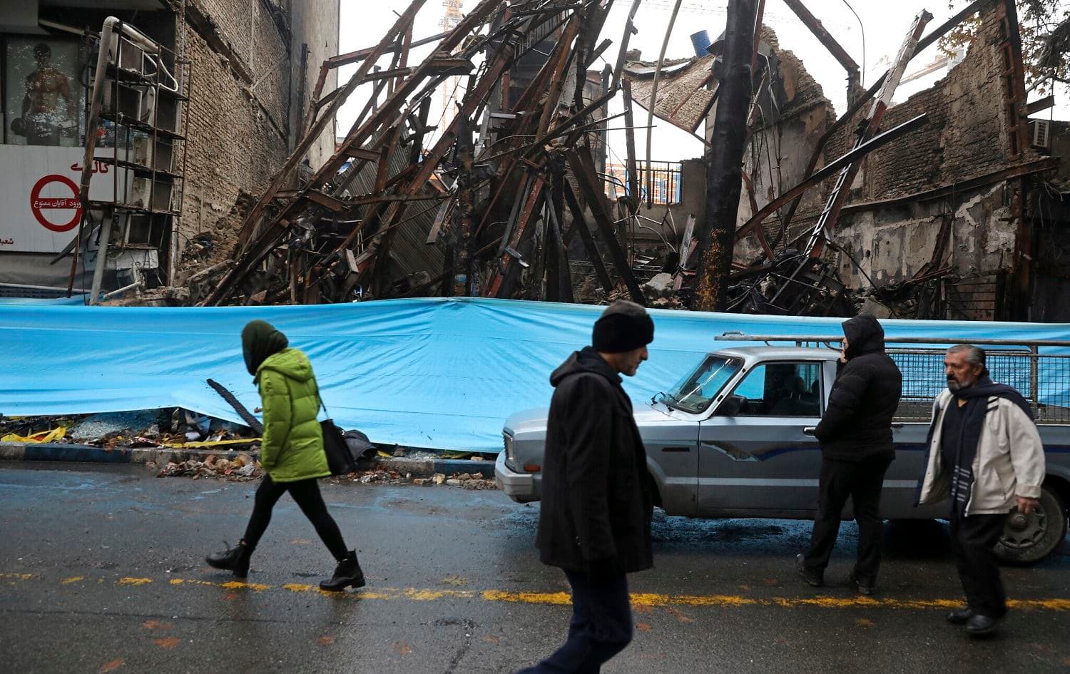 People walk past buildings that were burned during protests in Shahriar, Iran on November 20, 2019. Photo: Valid Salemi/AP