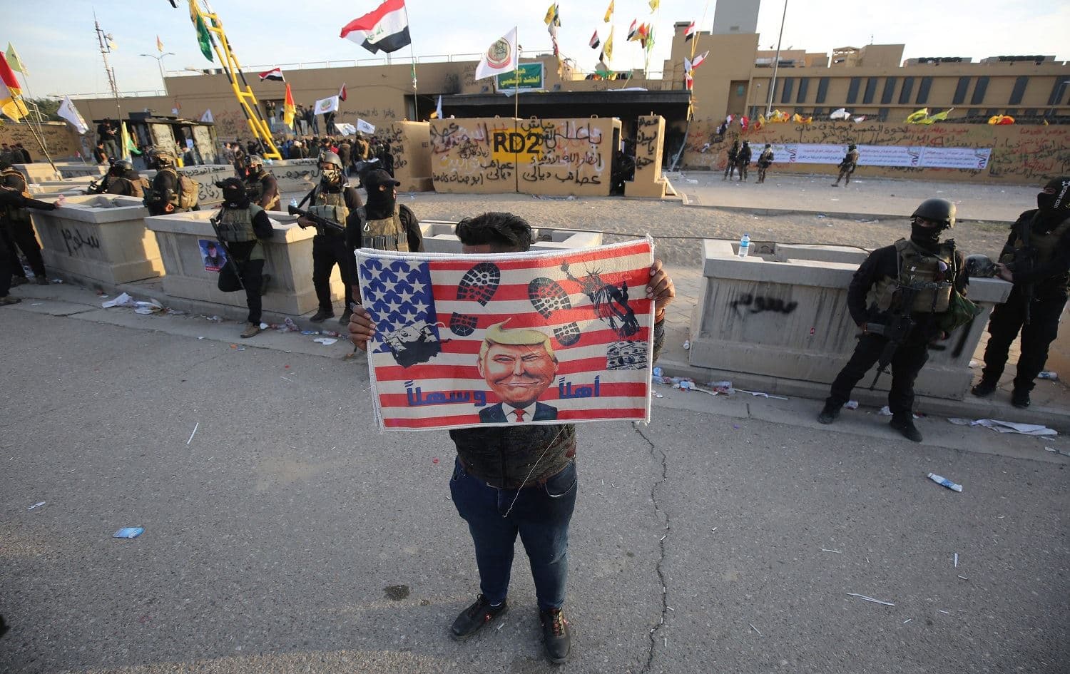 A supporter of Iraq's Hashd al-Shaabi paramilitary force holds a placard depicting trampled US symbols at the US Embassy in Baghdad on January 1, 2020. Photo: Ahmed al-Rubaye/AFP