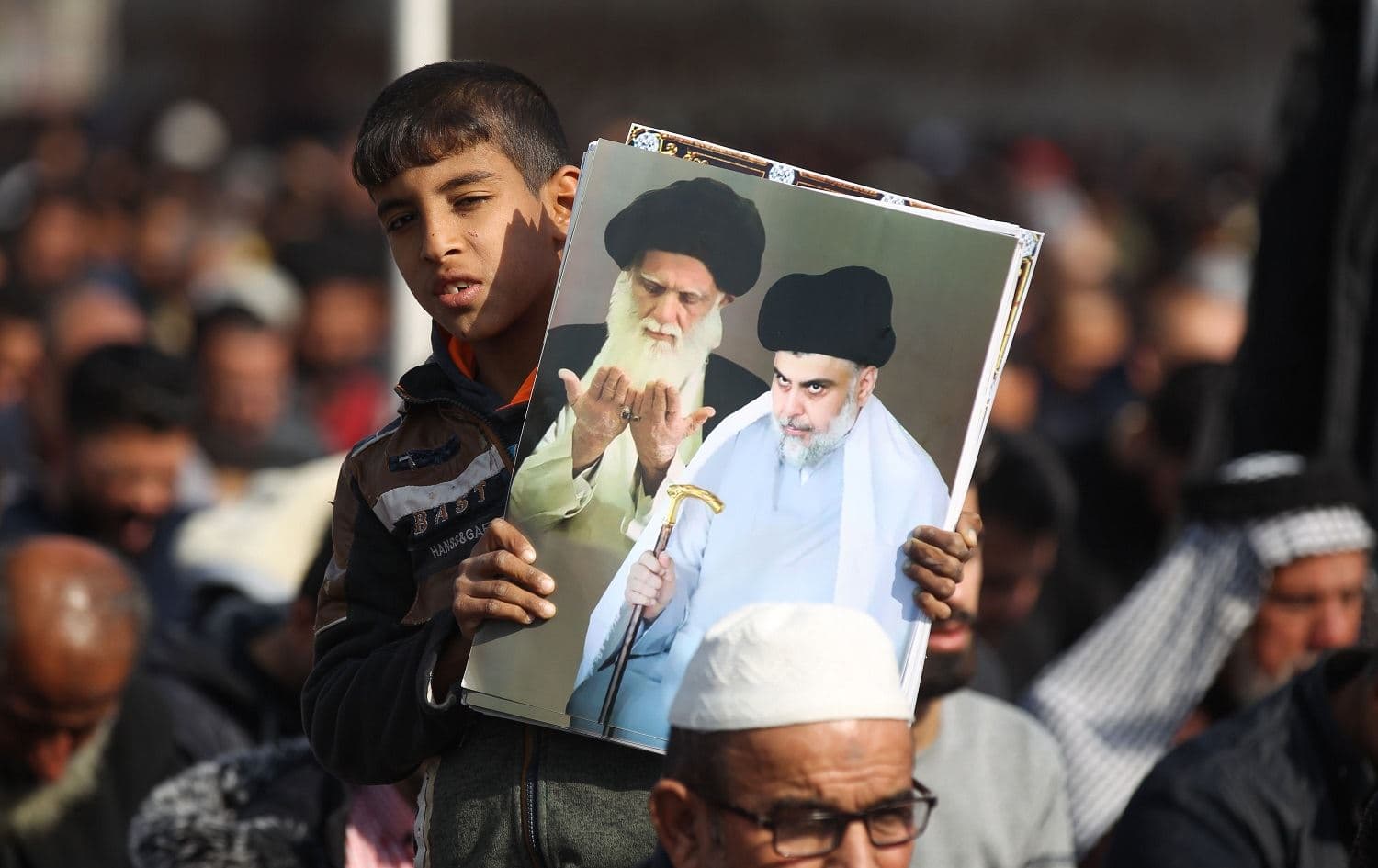 A young boy holds a poster showing top Shiite cleric Grand Ayatollah Ali Sistani (left) and Shiite cleric Moqtada al-Sadr as supporters of the latter take part in Friday prayers in Sadr City, Baghdad on January 3, 2020. Photo: Ahmad al-Rubaye / AFP
