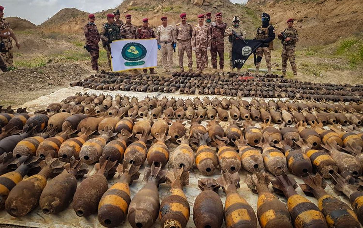 Iraqi Security Forces (ISF) pose with a captured Islamic State (ISIS) flag and explosives uncovered in al-Qaim, near the Iraq-Syria border, April 3, 2020. Photo: Iraqi defense ministry / social media