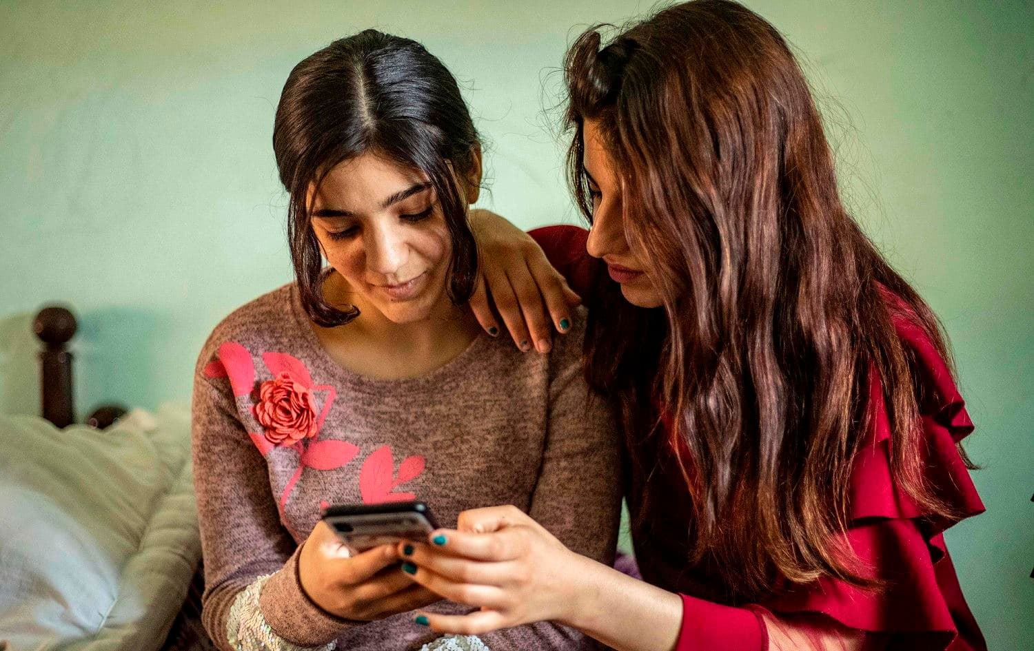 Layla Eido (L), a teenager from Iraq's minority Yezidi community, looks at pictures with a friend in the countryside of Syria's northeastern province of Hasaka, April 23, 2020. Photo: Delil Souleiman / AFP