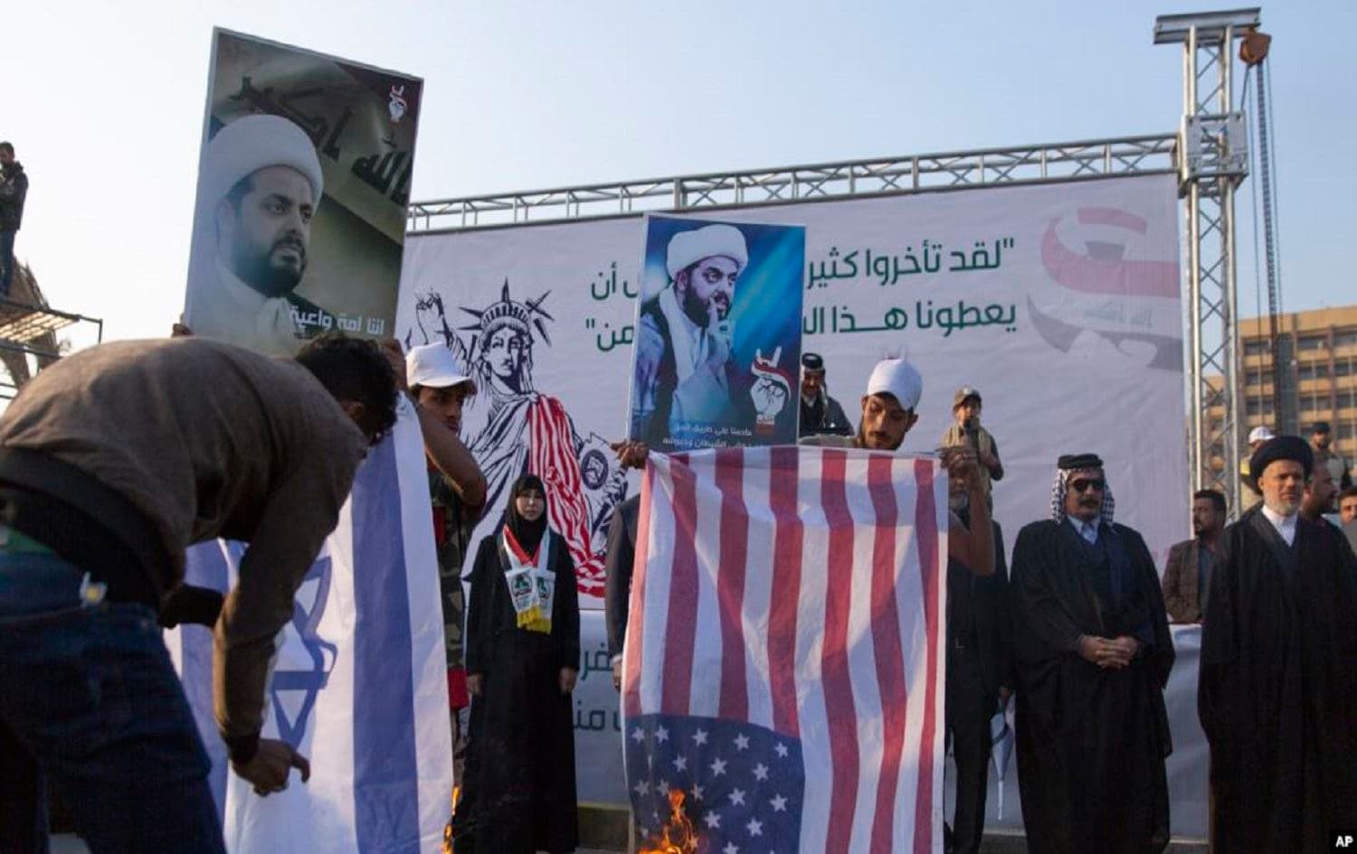Iraqi protesters burn Israeli and US flags while others carry posters with pictures of Qais al-Khazali, during a rally for the Shiite group Asaib Ahl al-Haq, in Baghdad, Iraq, Saturday, Dec. 14, 2019. Photo: Nasser Nasser / AP