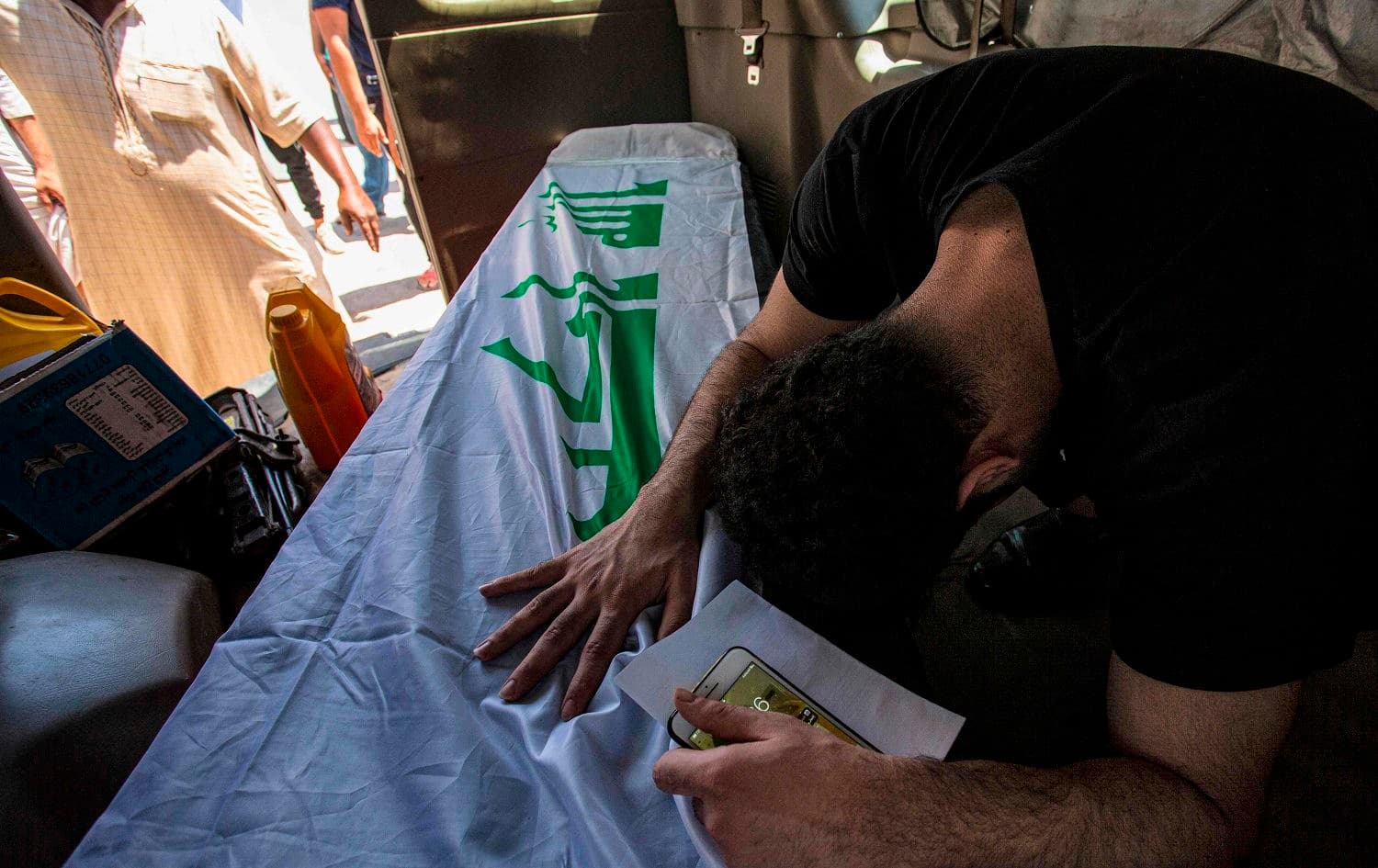A mourner reacts as he sits in the back of a vehicle by the Iraqi-flag draped coffin of slain activist Riham Yaaqub during her funeral in the centre of Iraq's southern city of Basra on August 20, 2020. Photo: Hussein Faleh/AFP