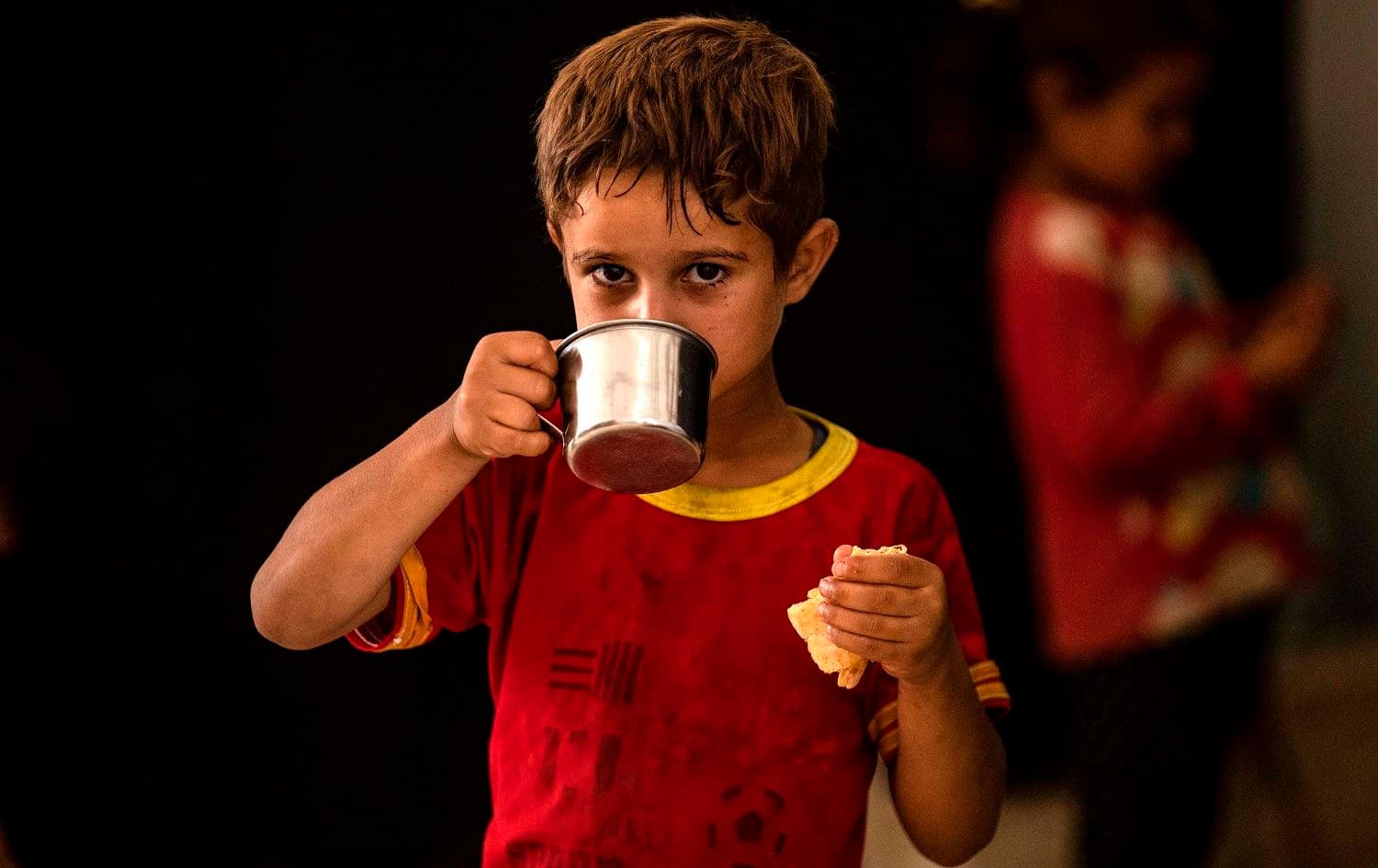 A boy drinks while holding a piece of bread inside a school building where Syrians displaced from Ras al-Ain, a border town controlled by Turkey and its Syrian proxies, are staying in the city of Hasaka on August 20, 2020. Photo: Delil Souleiman/AFP