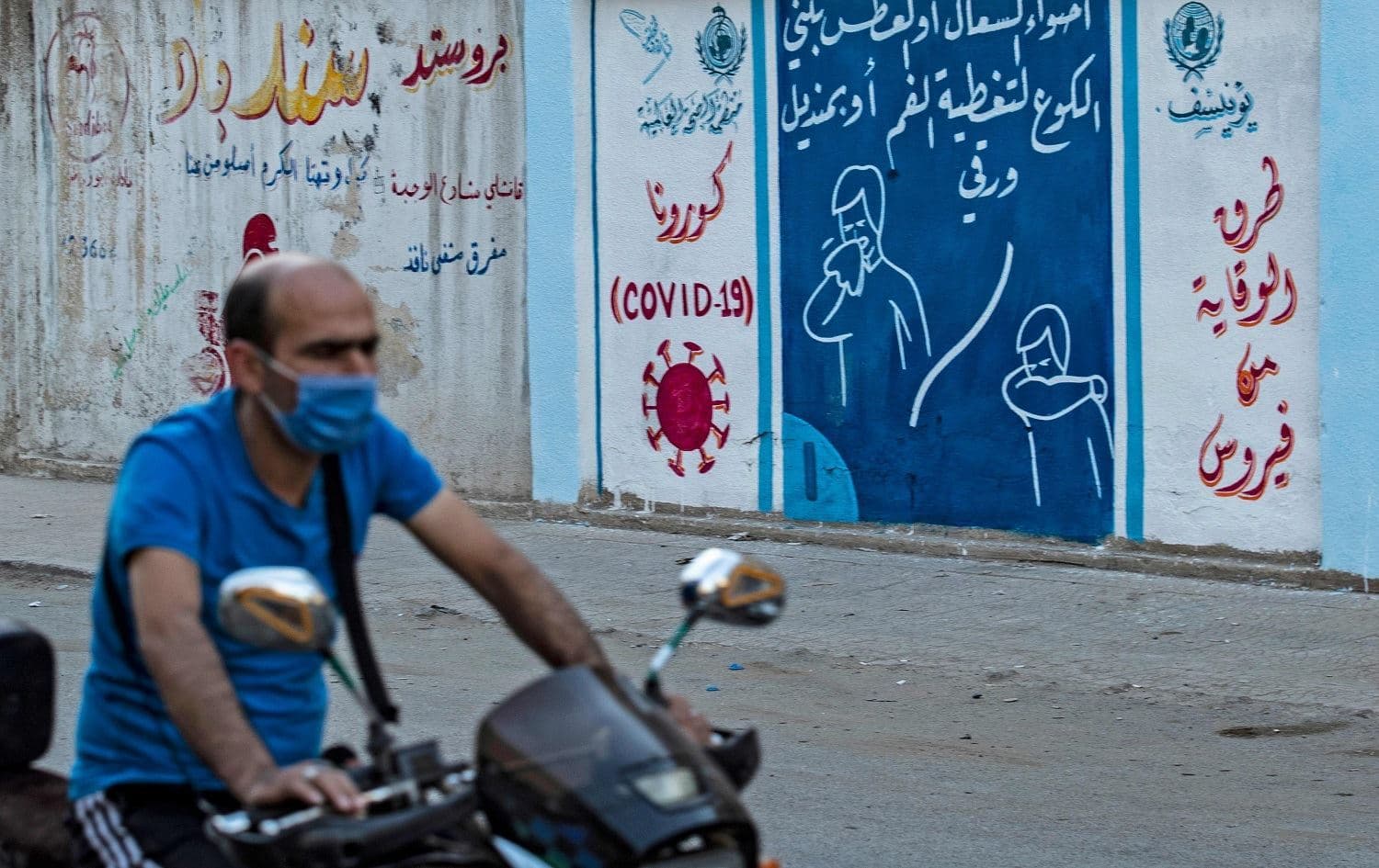A motorcyclist rides by a mural painted as part of an awareness campaign about the coronavirus in Qamishli in August 2020. File photo: Delil Souleiman/AFP