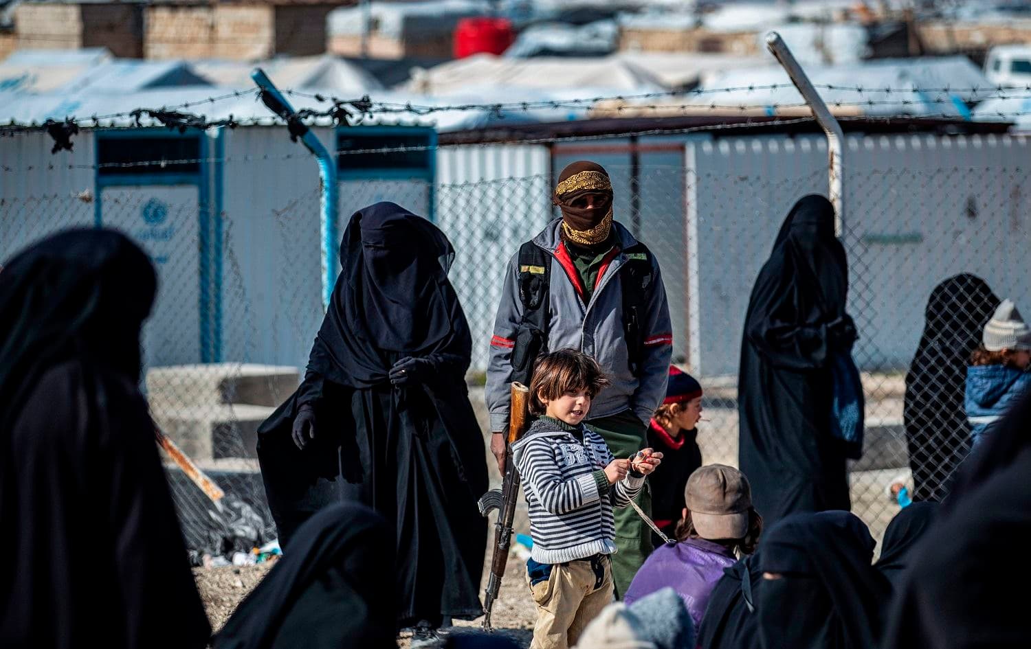 A member of Kurdish internal security stands guard as women lead children ahead of departure during the release of another group of Syrian families from al-Hol in Hasaka governorate, northeastern Syria on January 28, 2021. Photo Delil Souleiman/AFP