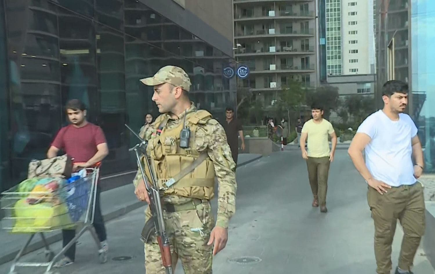 People walk past a member of the security forces where two people were injured by gunfire in front of a busy apartment complex in Erbil on May 1, 2021. Photo: Rudaw