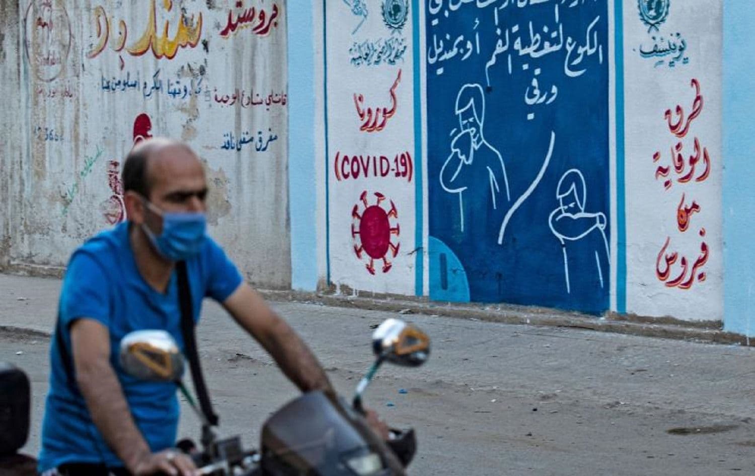 A Syrian man rides a motorbike past a mural painted as part of an awareness campaign by the United Nations International Children's Emergency Fund (UNICEF) and World Health Organization (WHO) intitative in Qamishli on Aug. 16, 2020, after a spike in infections in the area. - Delil Souleiman/AFP via Getty Images