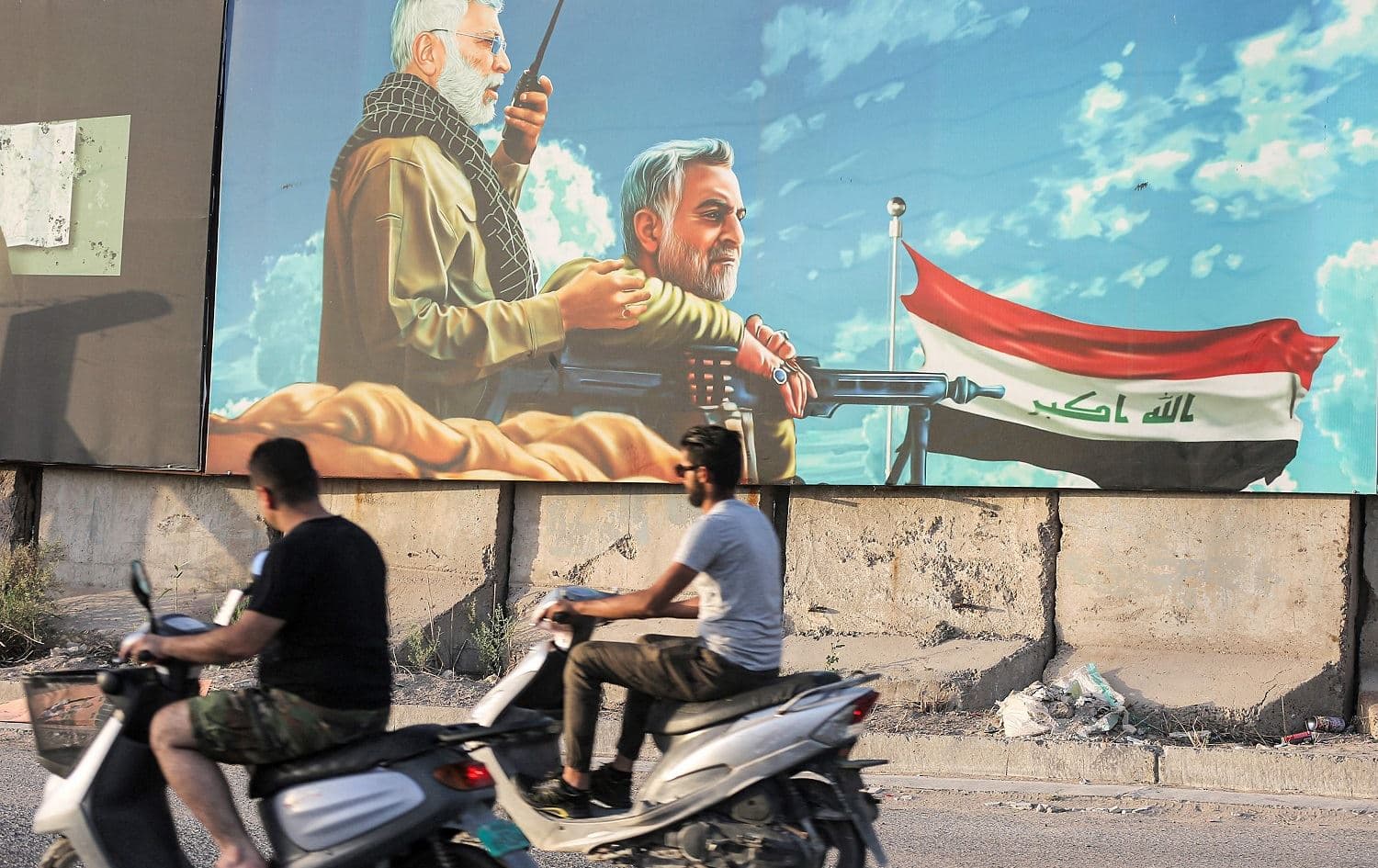 Men ride scooters in Baghdad on June 13, 2021 past a billboard depicting (L to R) the late commander of the Iranian-backed PMF Abu Mahdi al-Muhandis and Iran's Revolutionary Guards commander Qasem Soleimani, who were both assassinated together in January 2020. Photo: Ahmad al-Rubaye/AFP