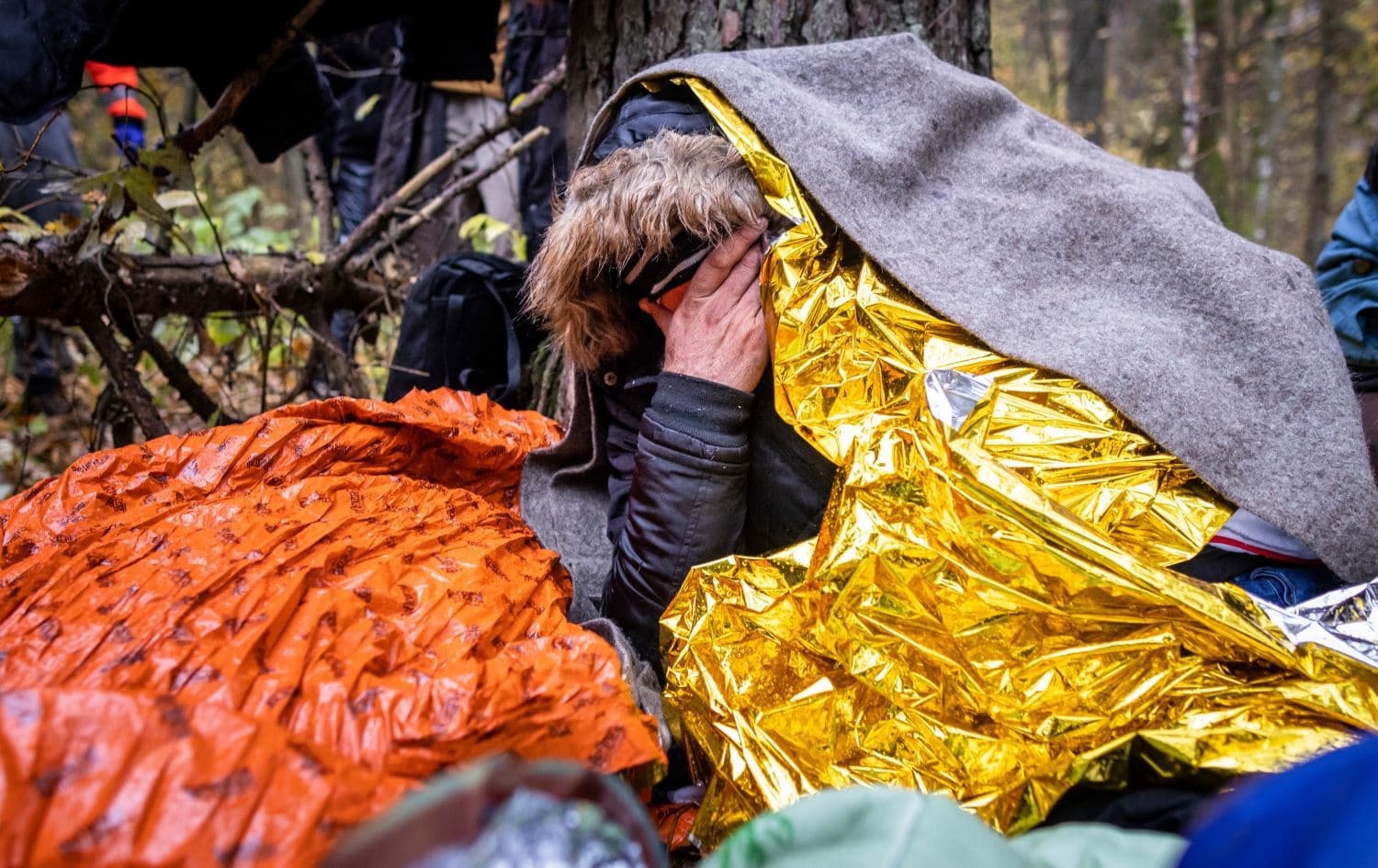 A migrant sits under rescue blankets to protect against the rain in the forest near Hajnowka, Poland, during a joint rescue operation of activists on October 23, 2021. Photo: Wojtek RADWANSKI / AFP