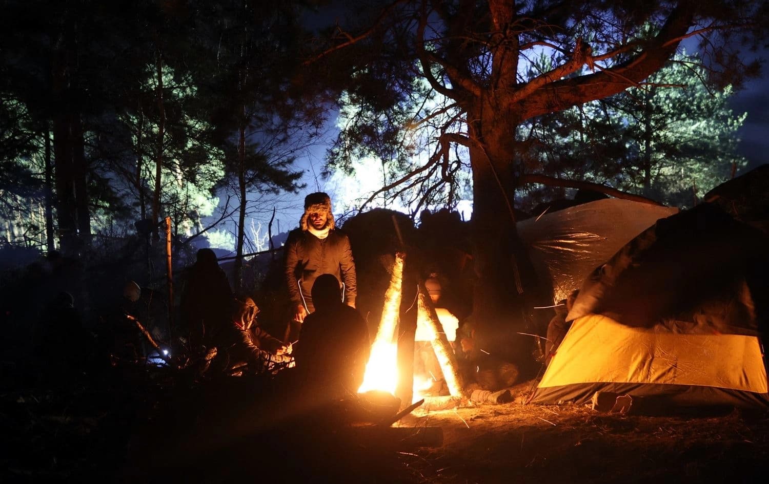 A group of migrants rest by a fire at a camp near the Belarusian-Polish border in the Grodno region on November 13, 2021. Photo: Leonid Shchleglov / AFP