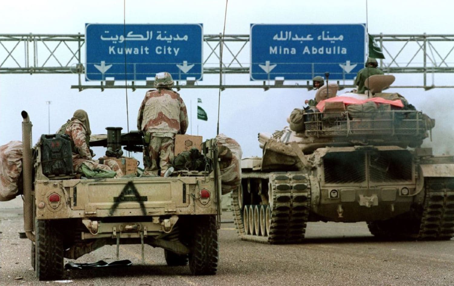 A U.S. Humvee and Saudi tank pass under a highway sign directing them to Kuwait City during Desert Storm Allied forces offensive in 1991. Photo: Christophe Simon/AFP