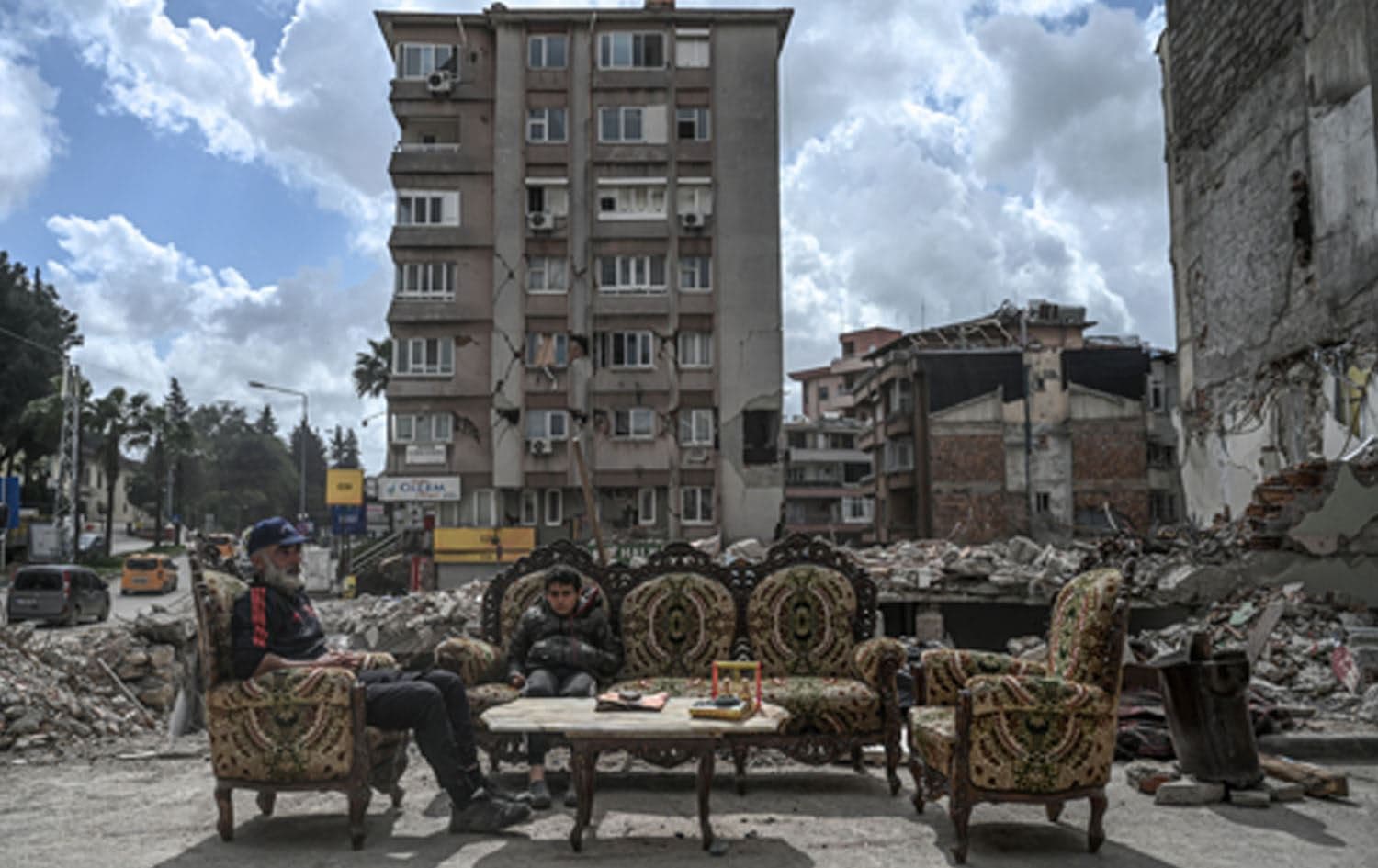 A man sits with his son amid the rubble of collapsed buildings, two months after a 7.8-magnitude jolt and its aftershocks wiped out swathes of Turkey's mountainous southeast, in Antakya on April 5, 2023. OZAN KOSE / AFP