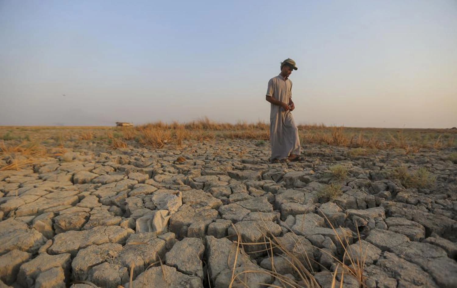 A fisherman walks across a dry patch of land in the marshes of southern Iraq which have suffered the consequences of back-to-back drought and rising salinity levels, in Dhi Qar province, Iraq, on 2 September, 2022. Photo: Anmar Khalil/AP
