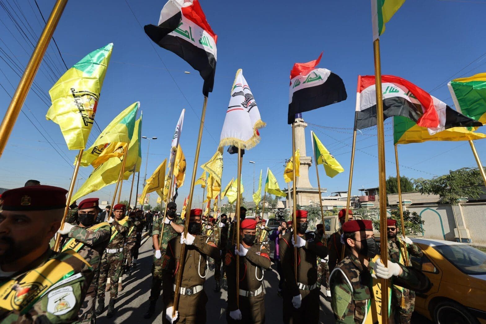Fighters lift flags of Iraq and paramilitary groups during a funeral in Baghdad following a US strike. Photo: Ahmad Al-Rubay/AFP
