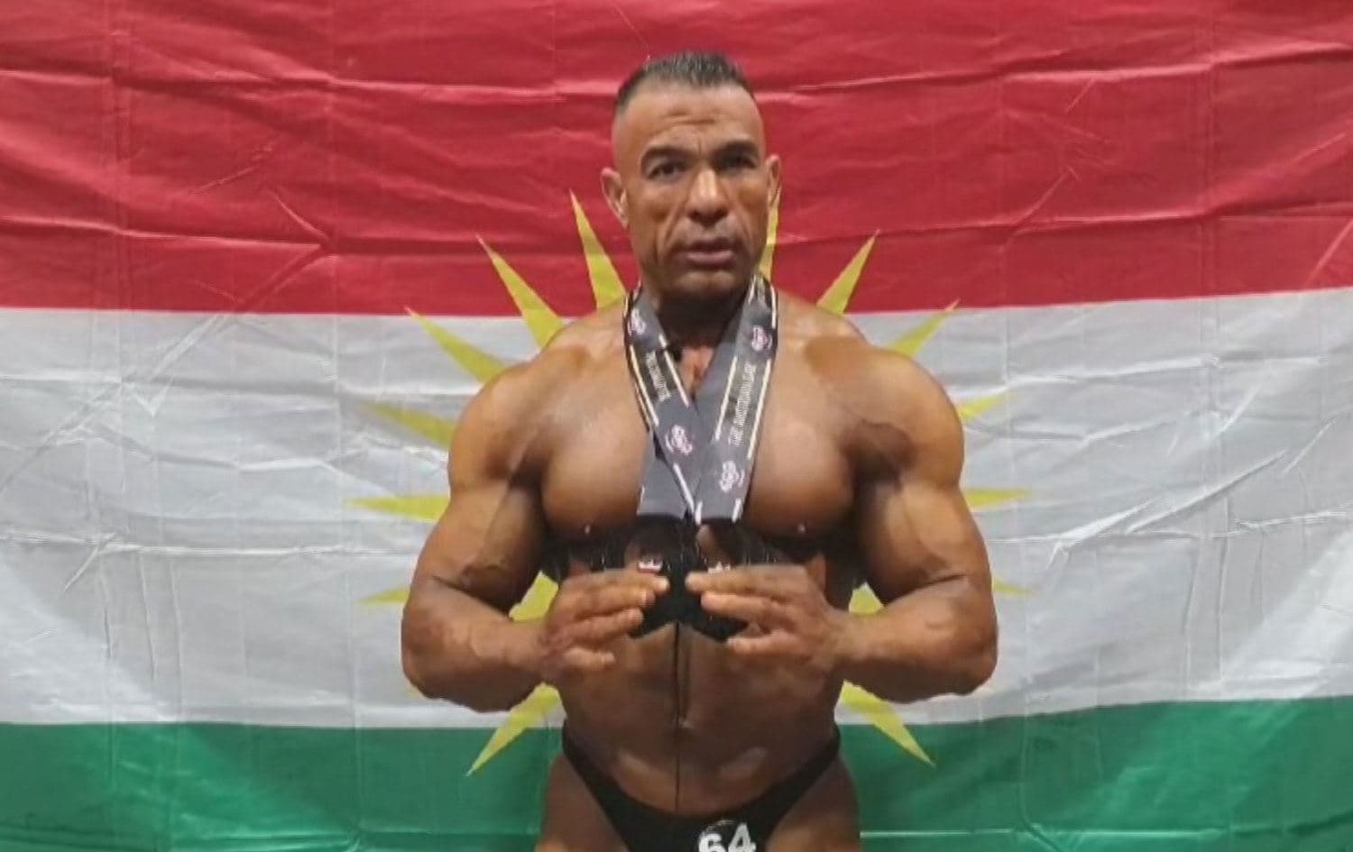 Abdulqadir Salih, a Kurdish bodybuilder from Sari Kani in Rojava, stands in front of the Flag of Kurdistan while holding his medals after a competition in Austria on August 25, 2024. Photo: submitted
