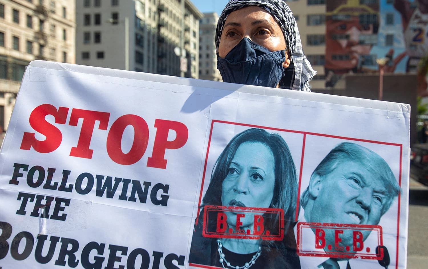 A protester holds a sign with pictures of Kamala Harris and Donald Trump reading "Stop Following the Bourgeois. File photo: AFP/Ringo Chiu